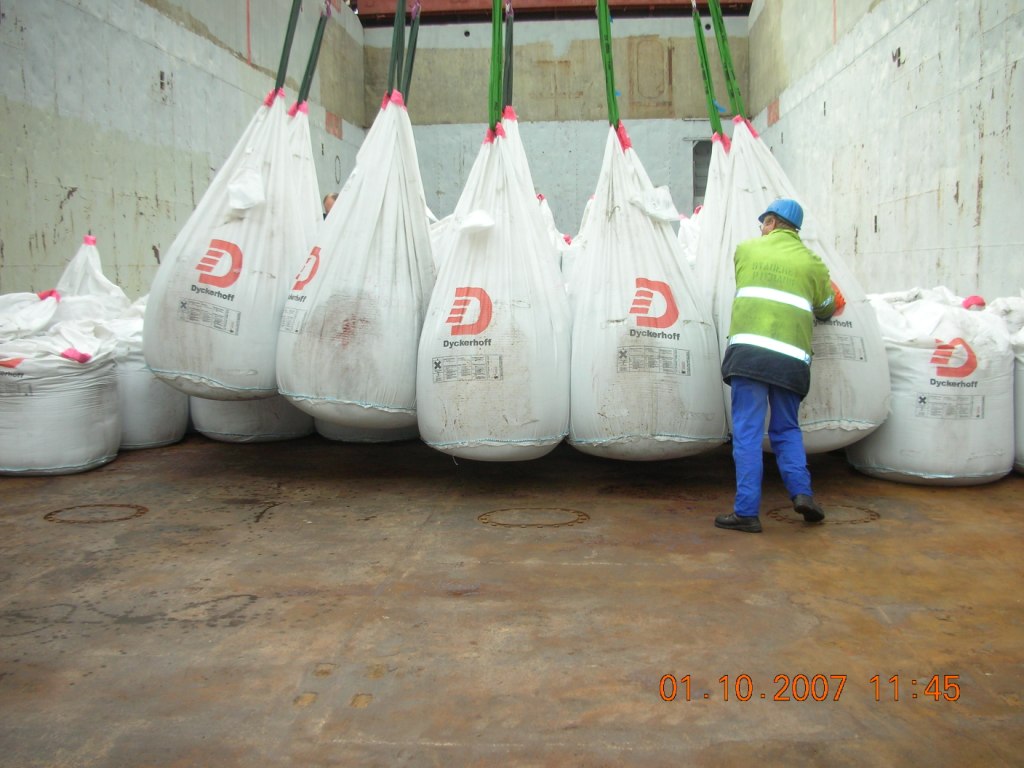 Duże worki z cementem 42.5 I, zawieszone na hakach wewnątrz statku, z pracownikiem w odblaskowej kamizelce, przygotowującym je do rozładunku.